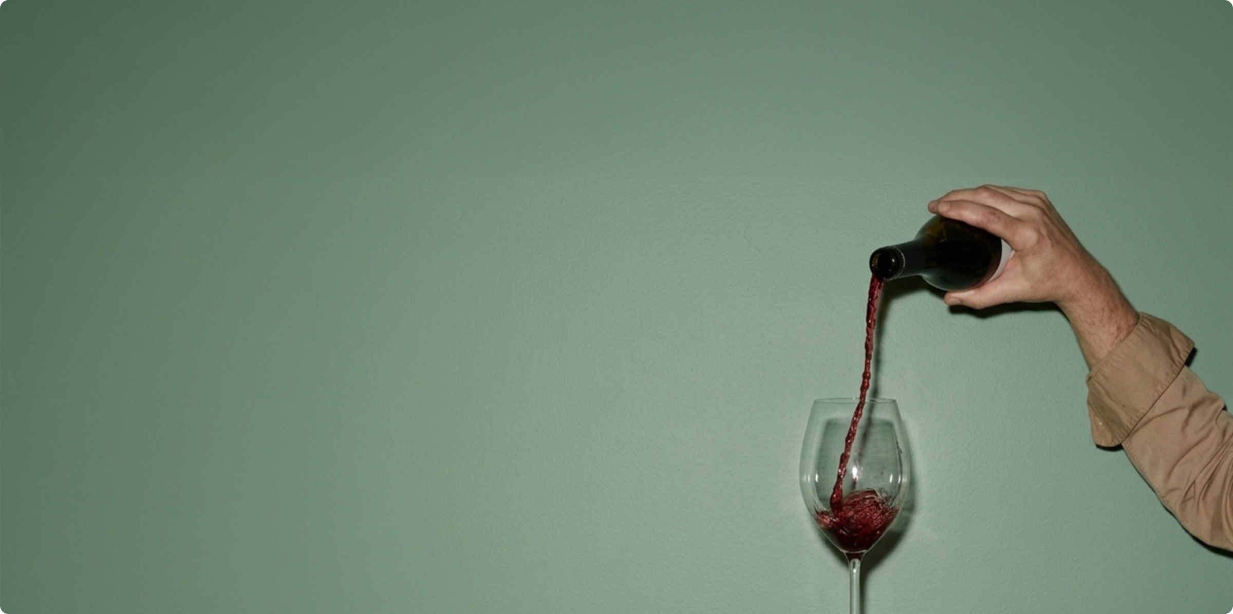 A glass of red wine being poured against a green wall